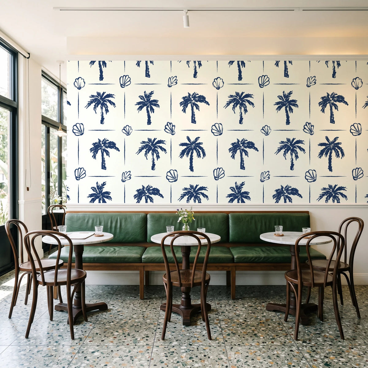 Ink & Shell Navy coastal palm and shell wallpaper above a green leather banquette in a sunlit neighborhood cafe