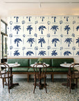 Ink & Shell Navy coastal palm and shell wallpaper above a green leather banquette in a sunlit neighborhood cafe