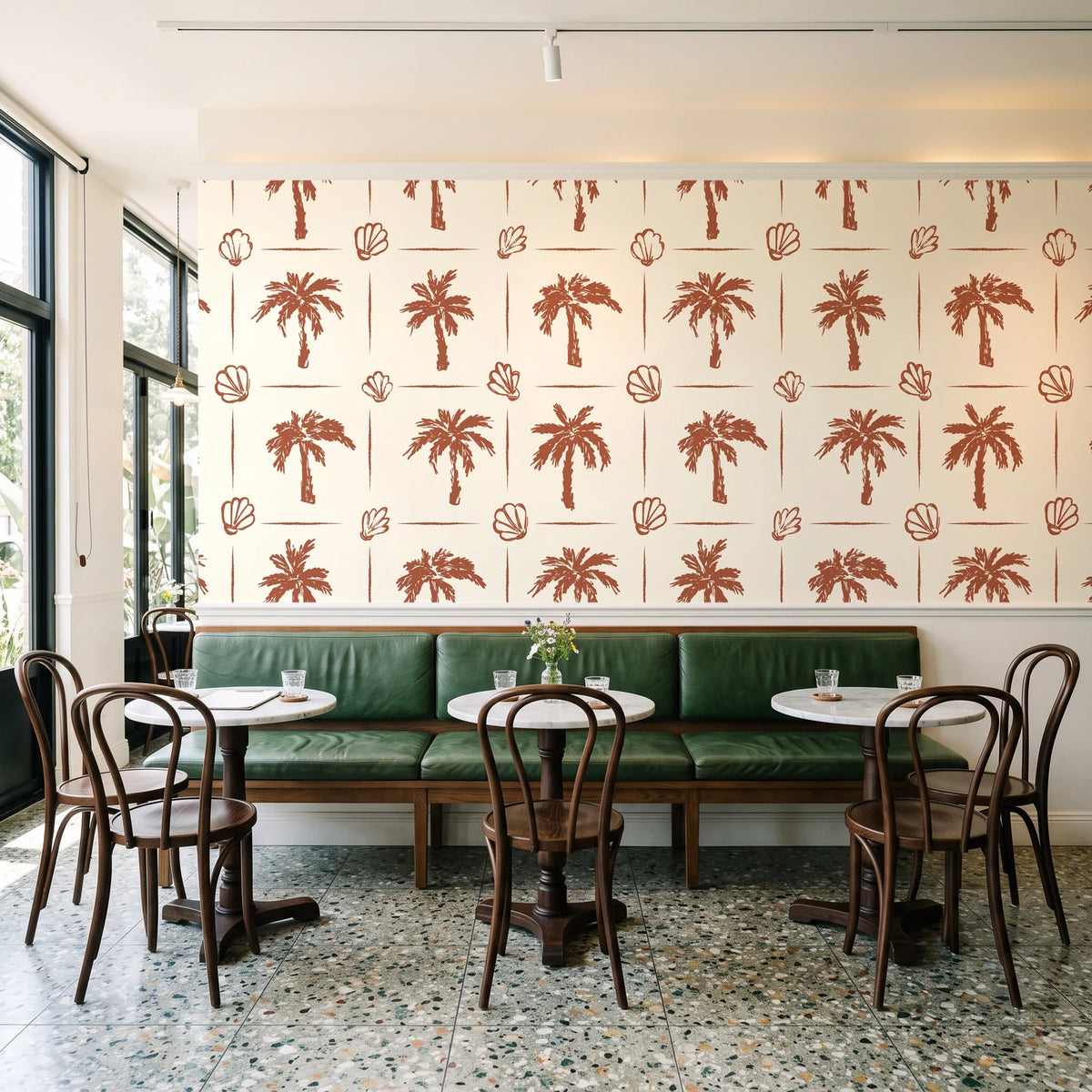 Ink & Shell Terracotta coastal palm and shell wallpaper above a green leather banquette in a sunlit neighborhood cafe