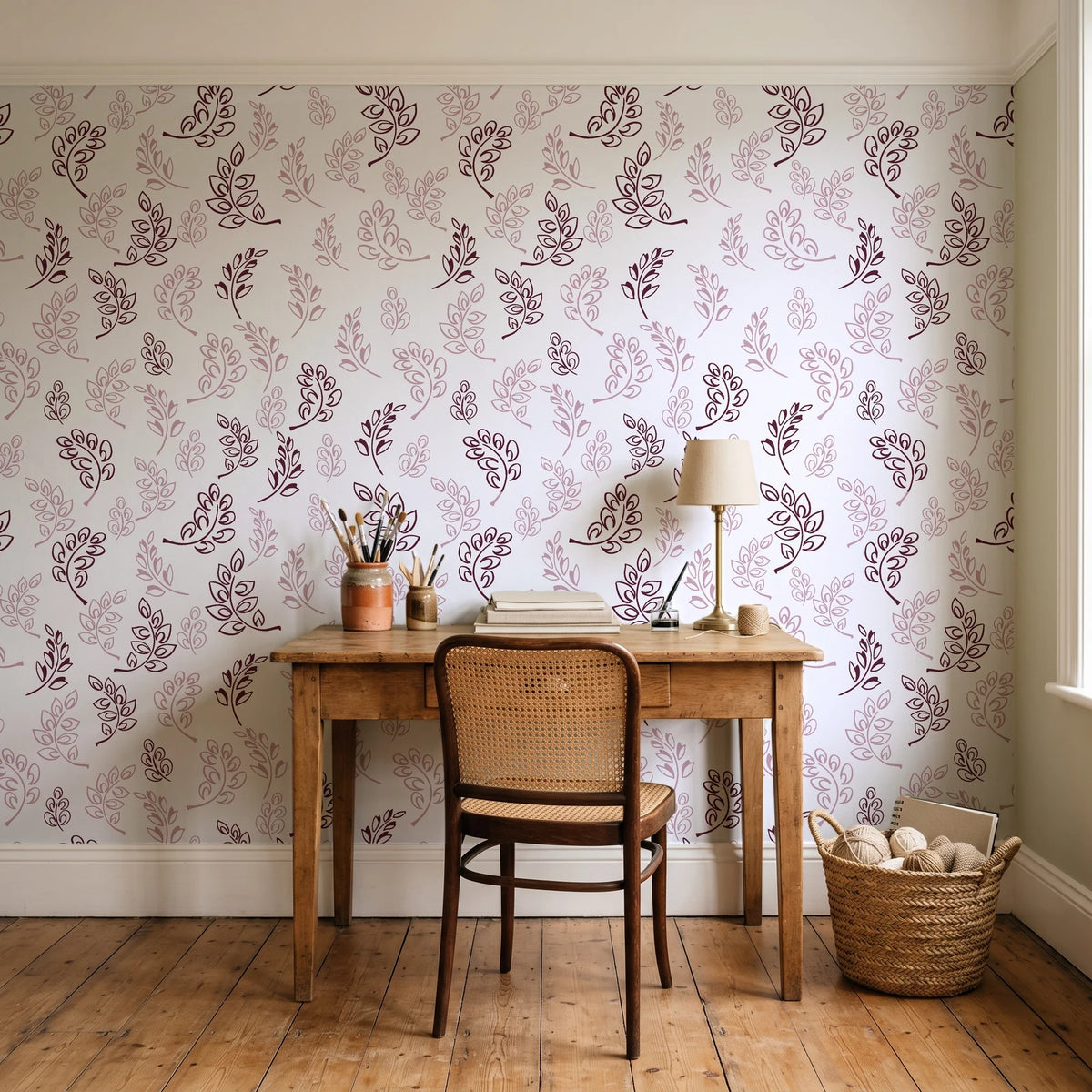 Ink & Sprig Burgundy botanical sprig wallpaper behind a vintage writing desk in a cozy craft-room home office