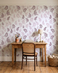 Ink & Sprig Burgundy botanical sprig wallpaper behind a vintage writing desk in a cozy craft-room home office