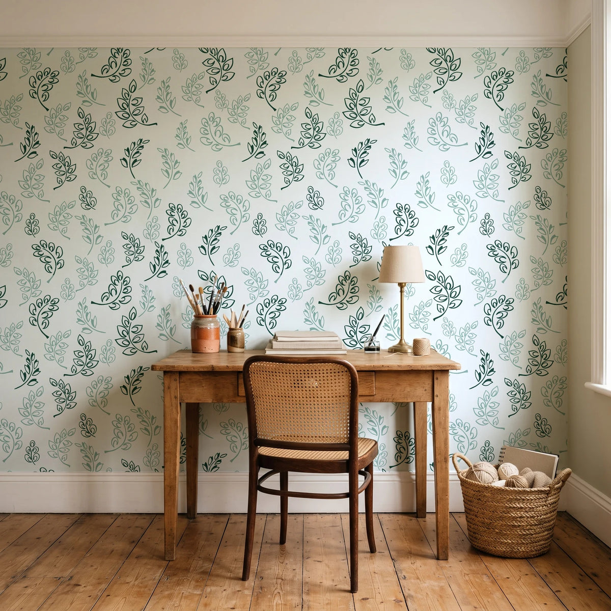 Ink & Sprig Emerald botanical sprig wallpaper behind a vintage writing desk in a cozy craft-room home office