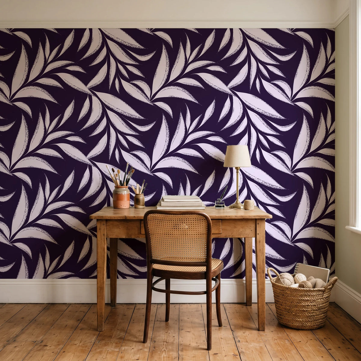 Ink Thicket Aubergine bold leaf wallpaper behind a vintage writing desk in a cozy craft-room home office