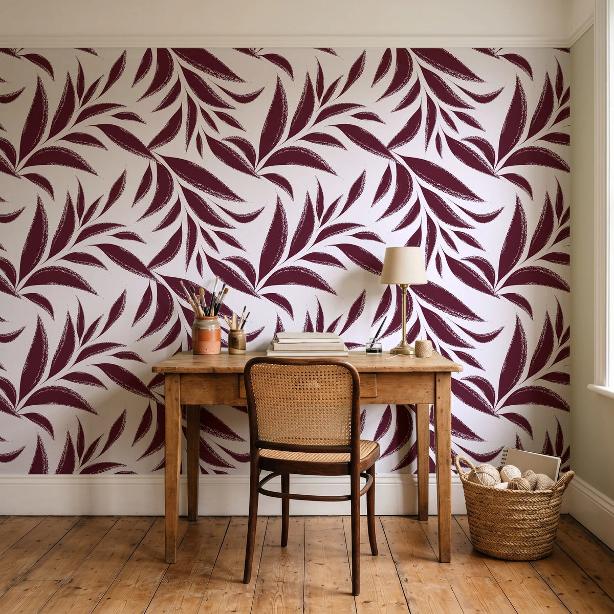 Ink Thicket Oxblood bold leaf wallpaper behind a vintage writing desk in a cozy craft-room home office