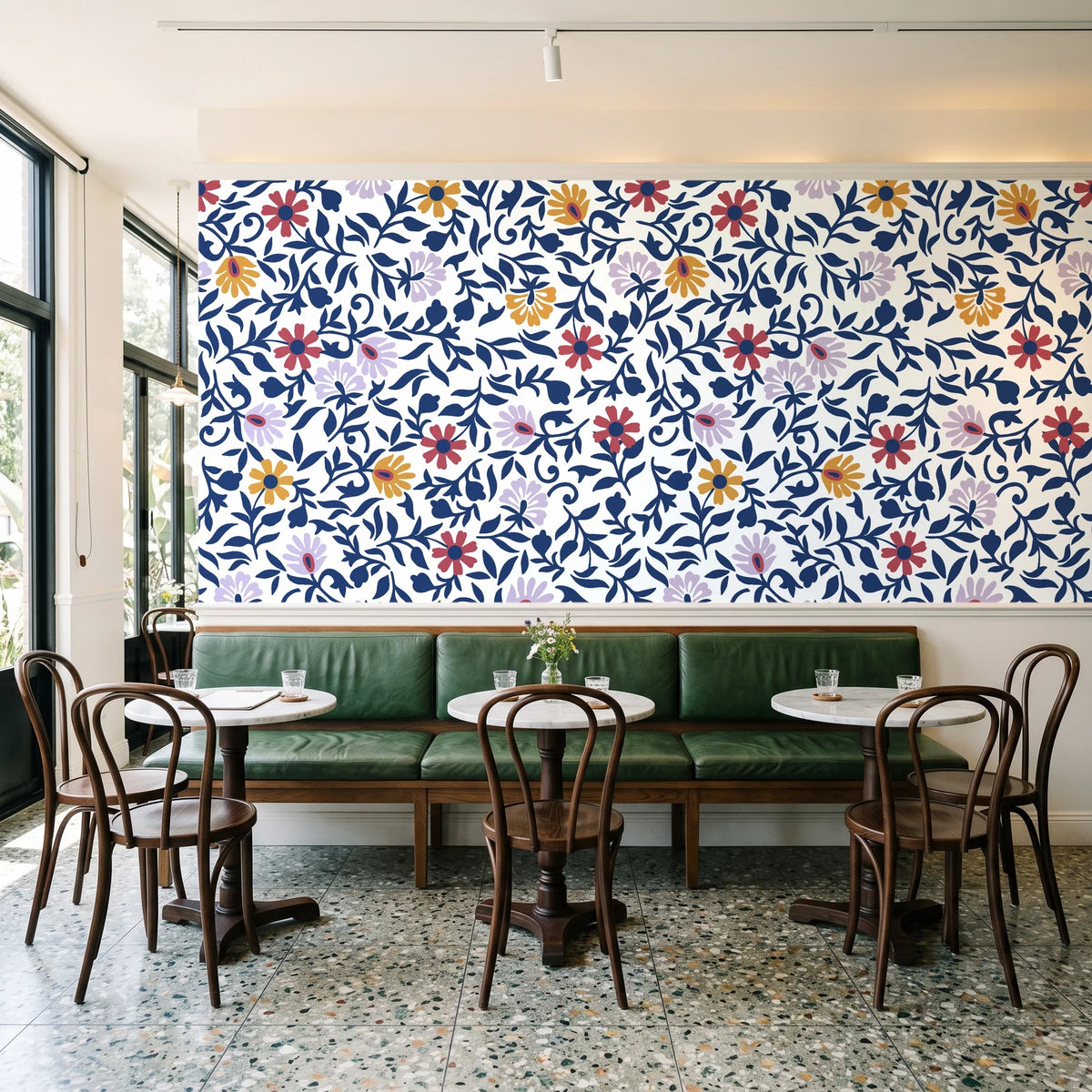 Matisse Reverie Navy folk floral wallpaper above a green leather banquette in a sunlit neighborhood cafe