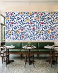 Matisse Reverie Navy folk floral wallpaper above a green leather banquette in a sunlit neighborhood cafe