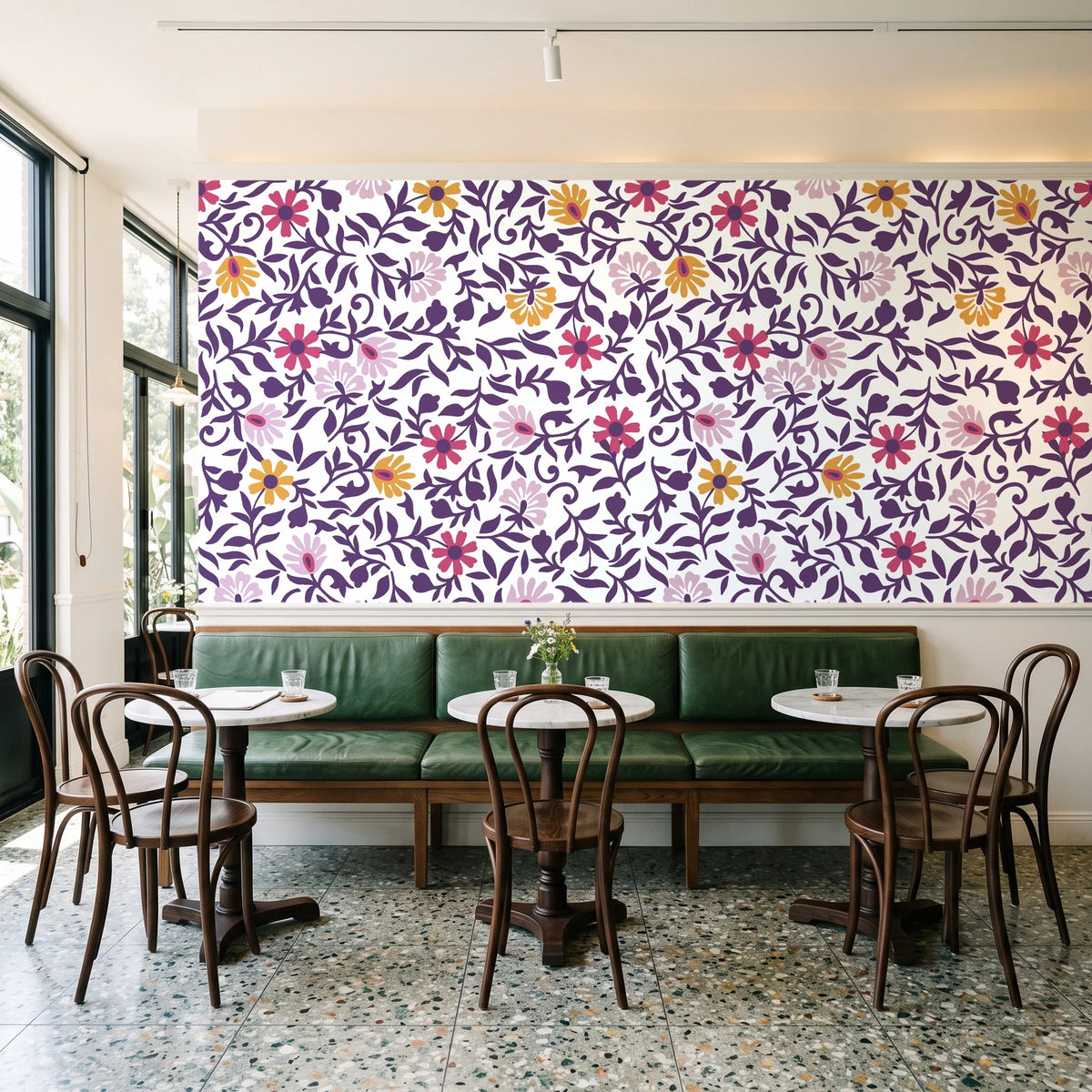 Matisse Reverie Plum folk floral wallpaper above a green leather banquette in a sunlit neighborhood cafe