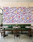 Matisse Reverie Plum folk floral wallpaper above a green leather banquette in a sunlit neighborhood cafe
