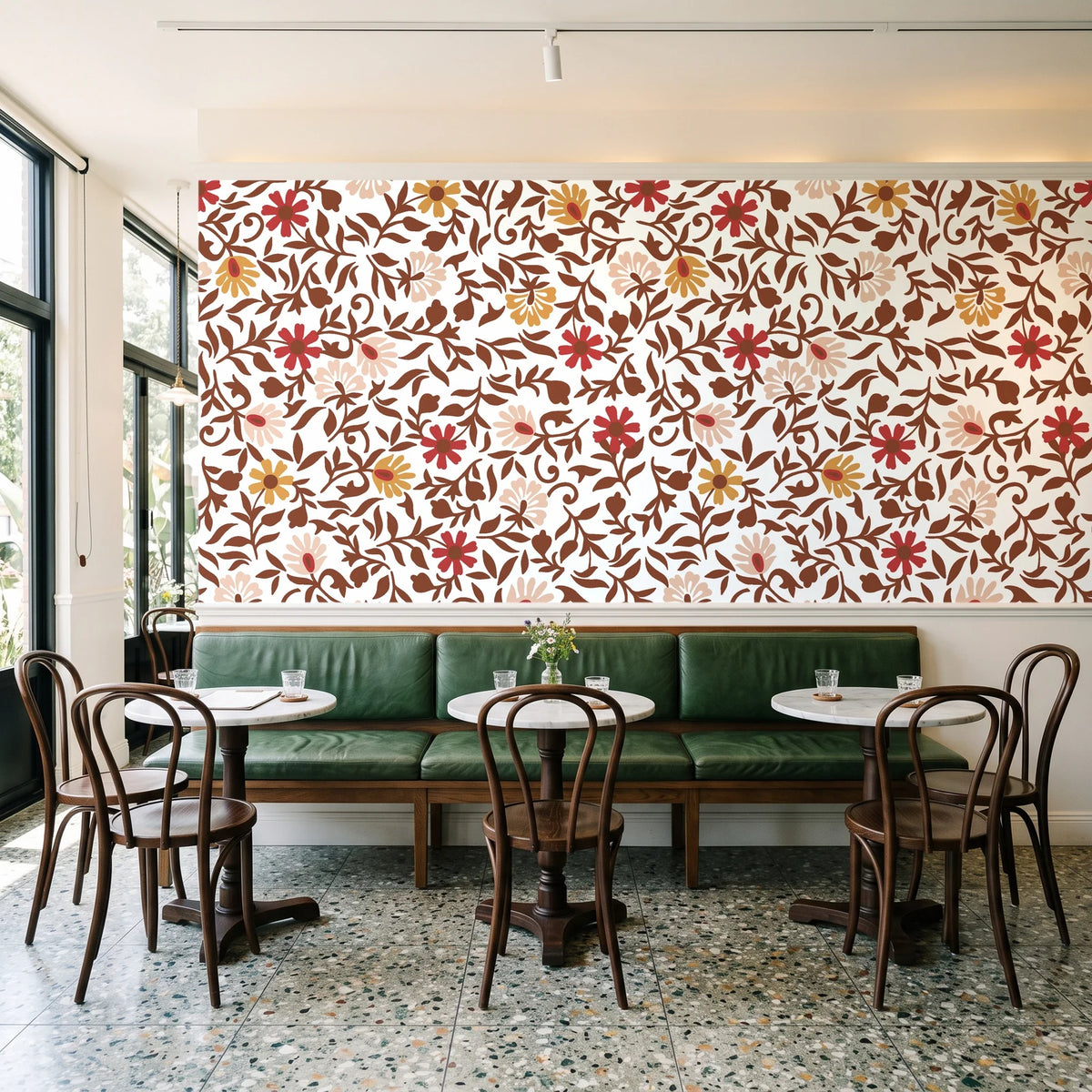 Matisse Reverie Rust folk floral wallpaper above a green leather banquette in a sunlit neighborhood cafe