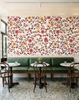 Matisse Reverie Rust folk floral wallpaper above a green leather banquette in a sunlit neighborhood cafe