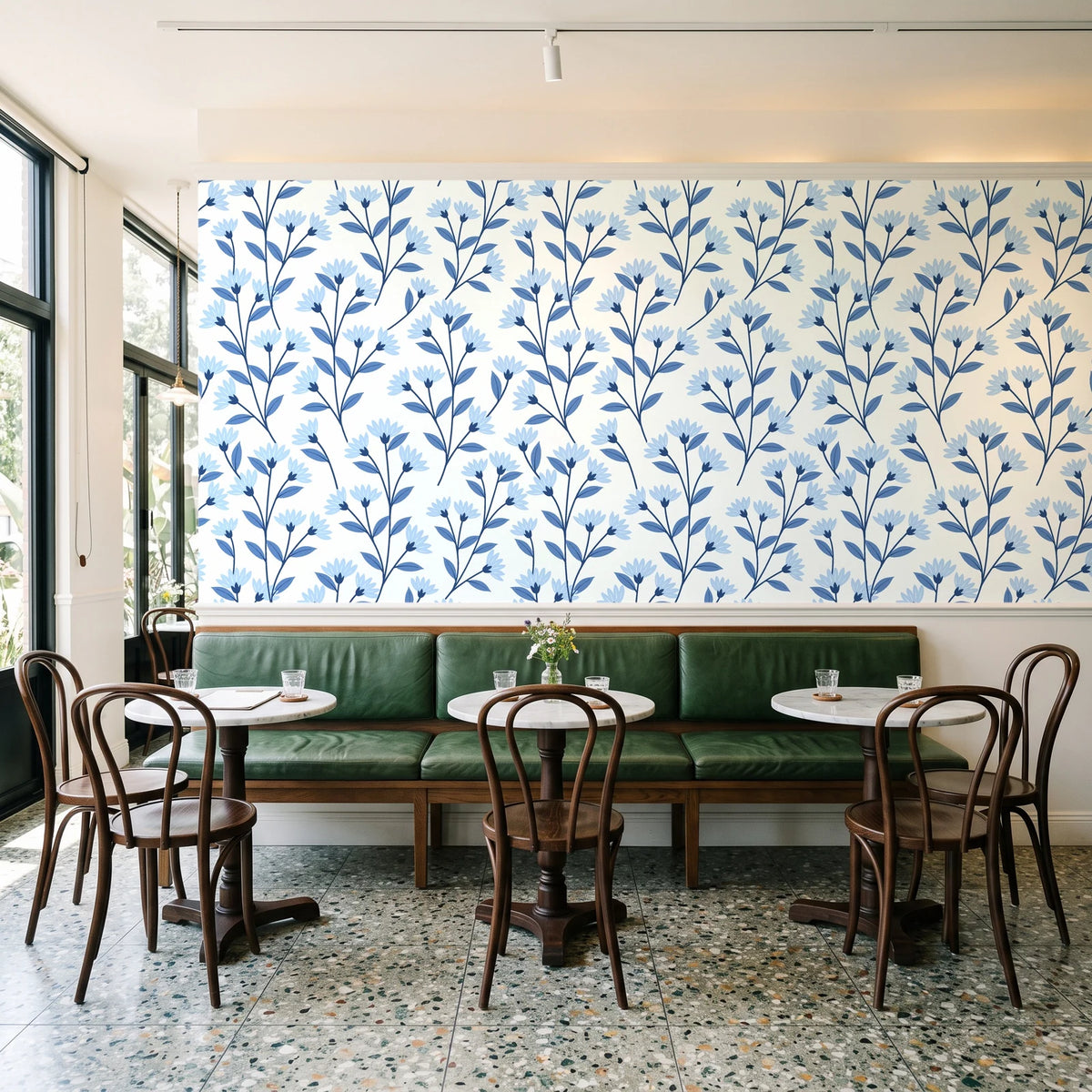 Meadow Light Cornflower meadow flower wallpaper above a green leather banquette in a sunlit neighborhood cafe