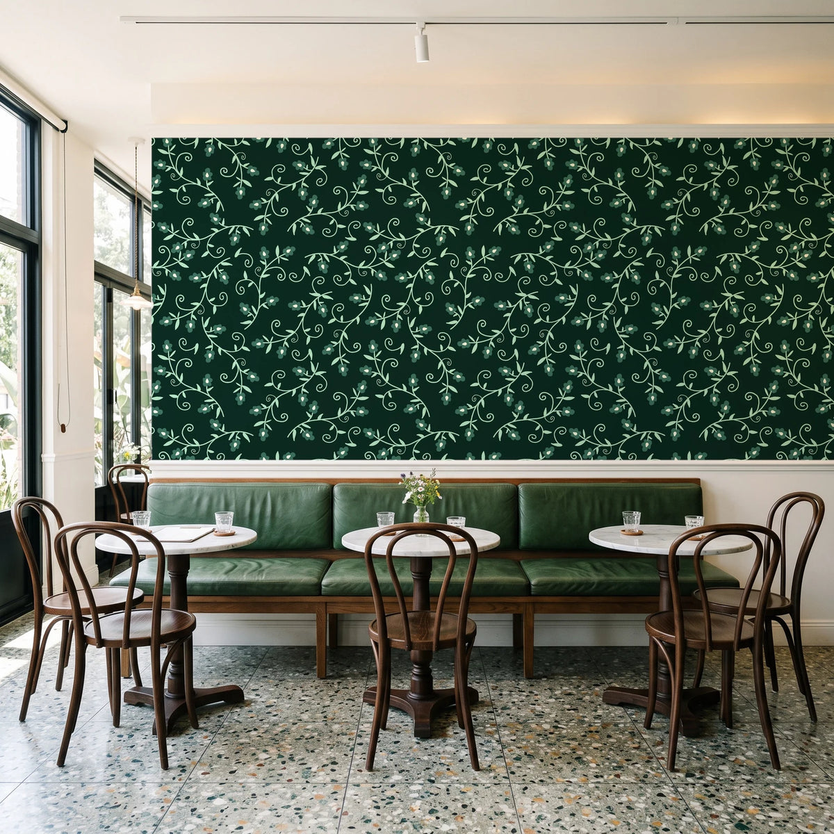 Meadow Wander Emerald floral vine wallpaper above a green leather banquette in a sunlit neighborhood cafe