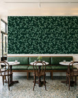 Meadow Wander Emerald floral vine wallpaper above a green leather banquette in a sunlit neighborhood cafe
