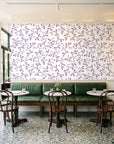 Meadow Wander Plum floral vine wallpaper above a green leather banquette in a sunlit neighborhood cafe