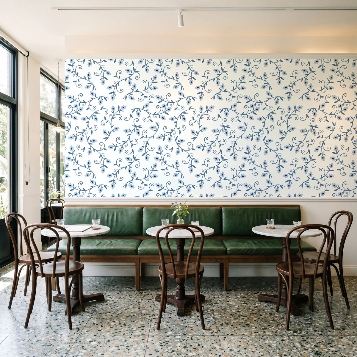 Meadow Wander Slate floral vine wallpaper above a green leather banquette in a sunlit neighborhood cafe