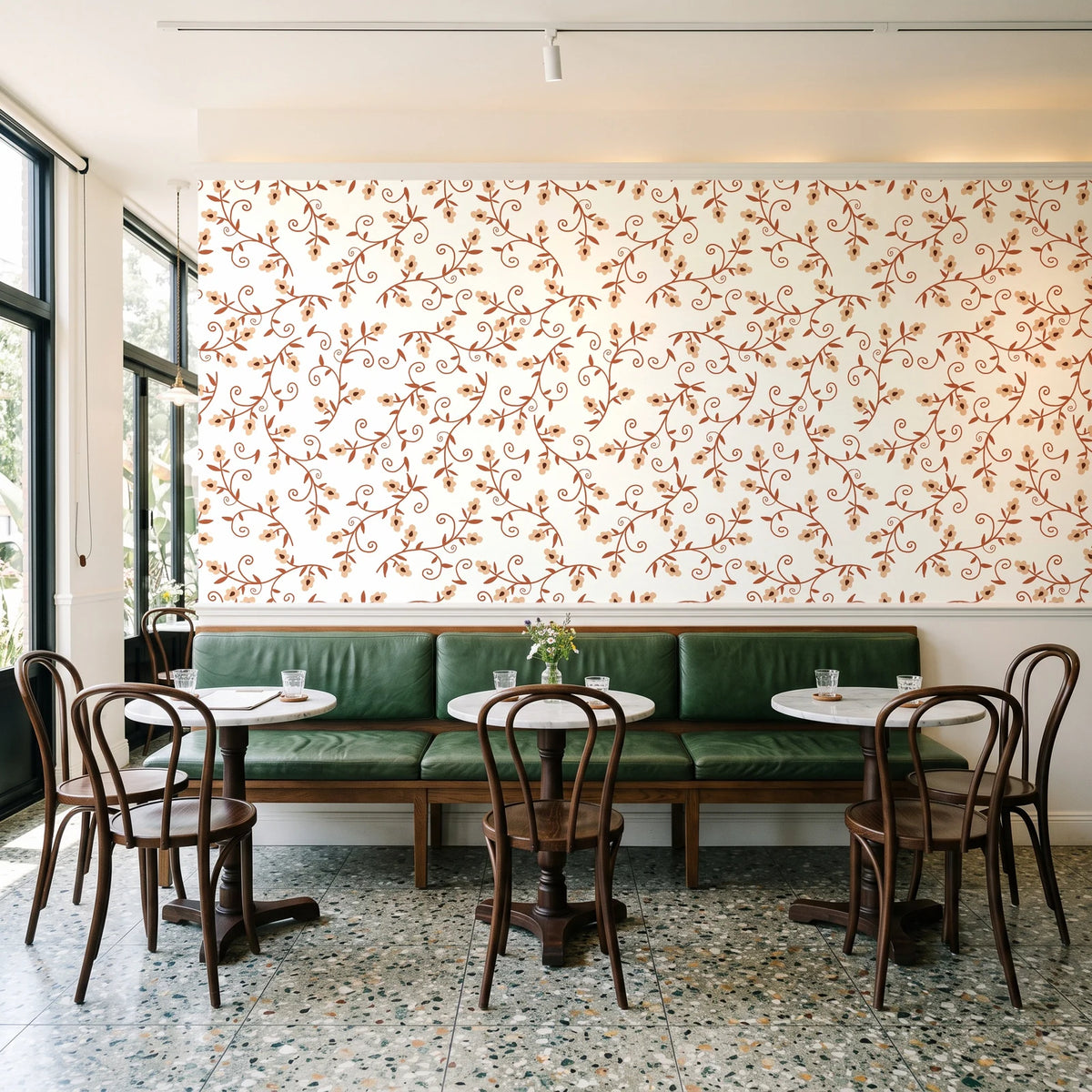 Meadow Wander Terracotta floral vine wallpaper above a green leather banquette in a sunlit neighborhood cafe
