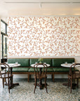 Meadow Wander Terracotta floral vine wallpaper above a green leather banquette in a sunlit neighborhood cafe