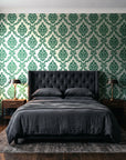 Misty Fern Romance Emerald damask wallpaper behind a tufted headboard in a dark, moody bedroom