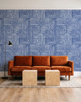 Nomad Stripe Indigo geometric wallpaper behind a rust velvet sofa in a bright coworking lounge