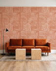 Nomad Stripe Terracotta geometric wallpaper behind a rust velvet sofa in a bright coworking lounge