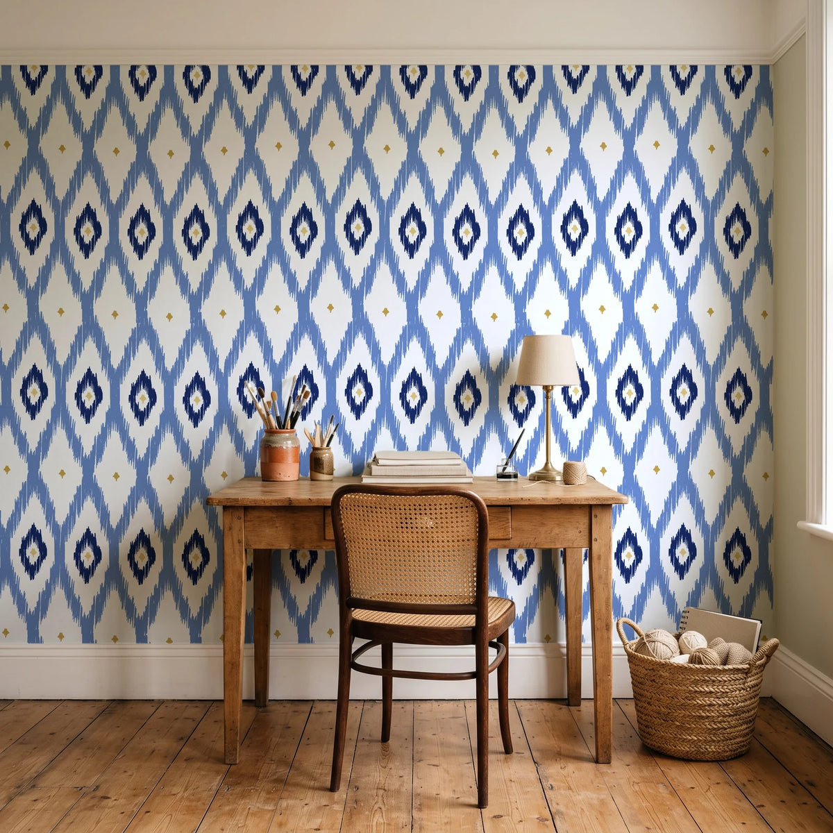 Ogee Loom Indigo ikat ogee wallpaper behind a vintage writing desk in a cozy craft-room home office