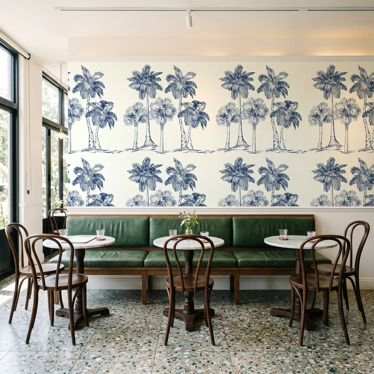 Palm Shade Navy palm grove wallpaper above a green leather banquette in a sunlit neighborhood cafe
