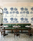 Palm Shade Navy palm grove wallpaper above a green leather banquette in a sunlit neighborhood cafe