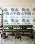 Palm Shade Slate palm grove wallpaper above a green leather banquette in a sunlit neighborhood cafe