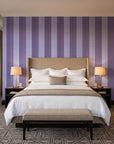 Parlor Stripe Plum geometric stripe wallpaper behind the headboard of a king bed in a contemporary hotel guest room