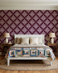 Pastel Bouquet Parade Oxblood botanical damask wallpaper behind a white cottage bed with a patchwork quilt in a cozy cottagecore bedroom