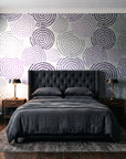 Petal Cascade Plum spiral rosette wallpaper behind a tufted headboard in a dark, moody bedroom