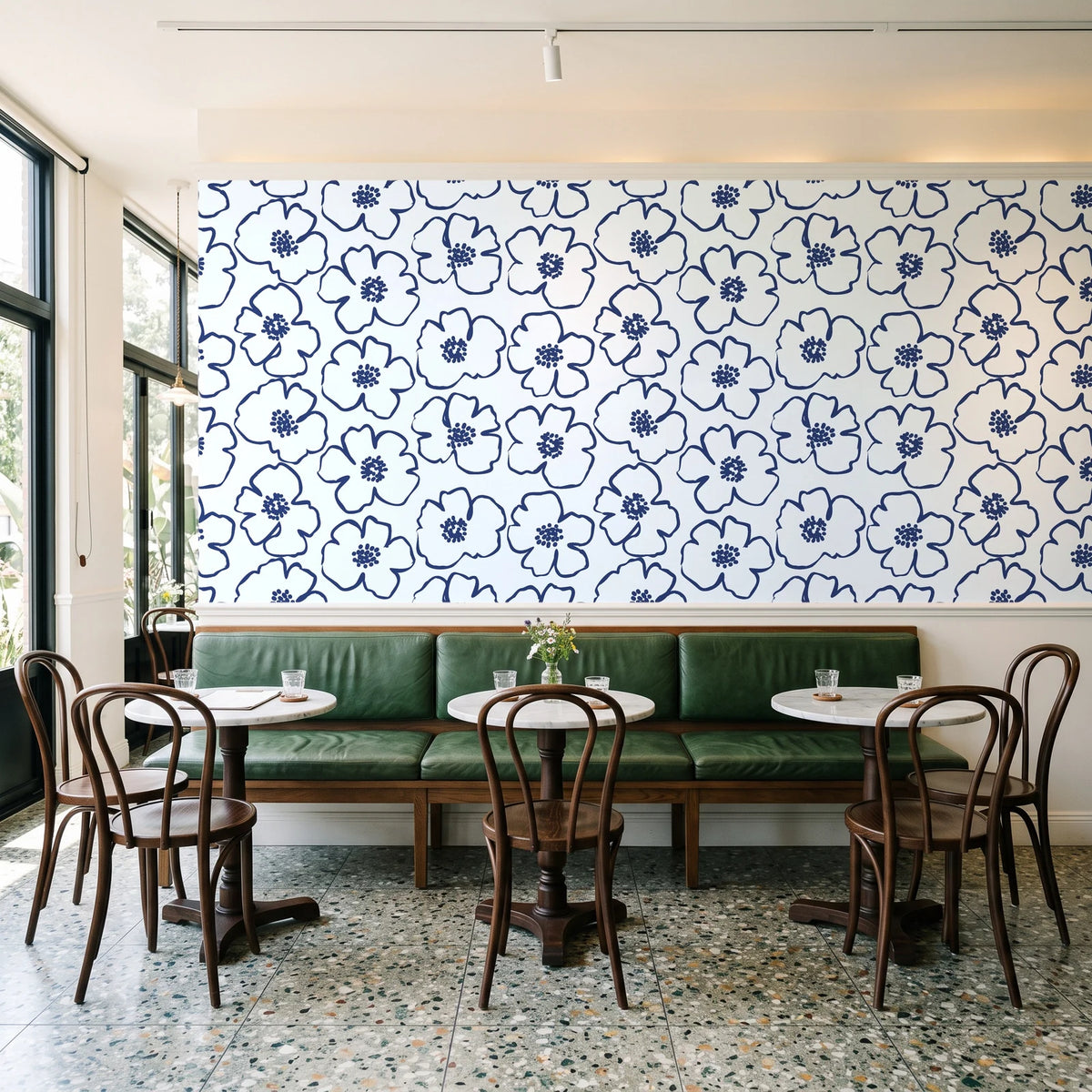 Sketch Anemone Indigo sketched anemone wallpaper above a green leather banquette in a sunlit neighborhood cafe