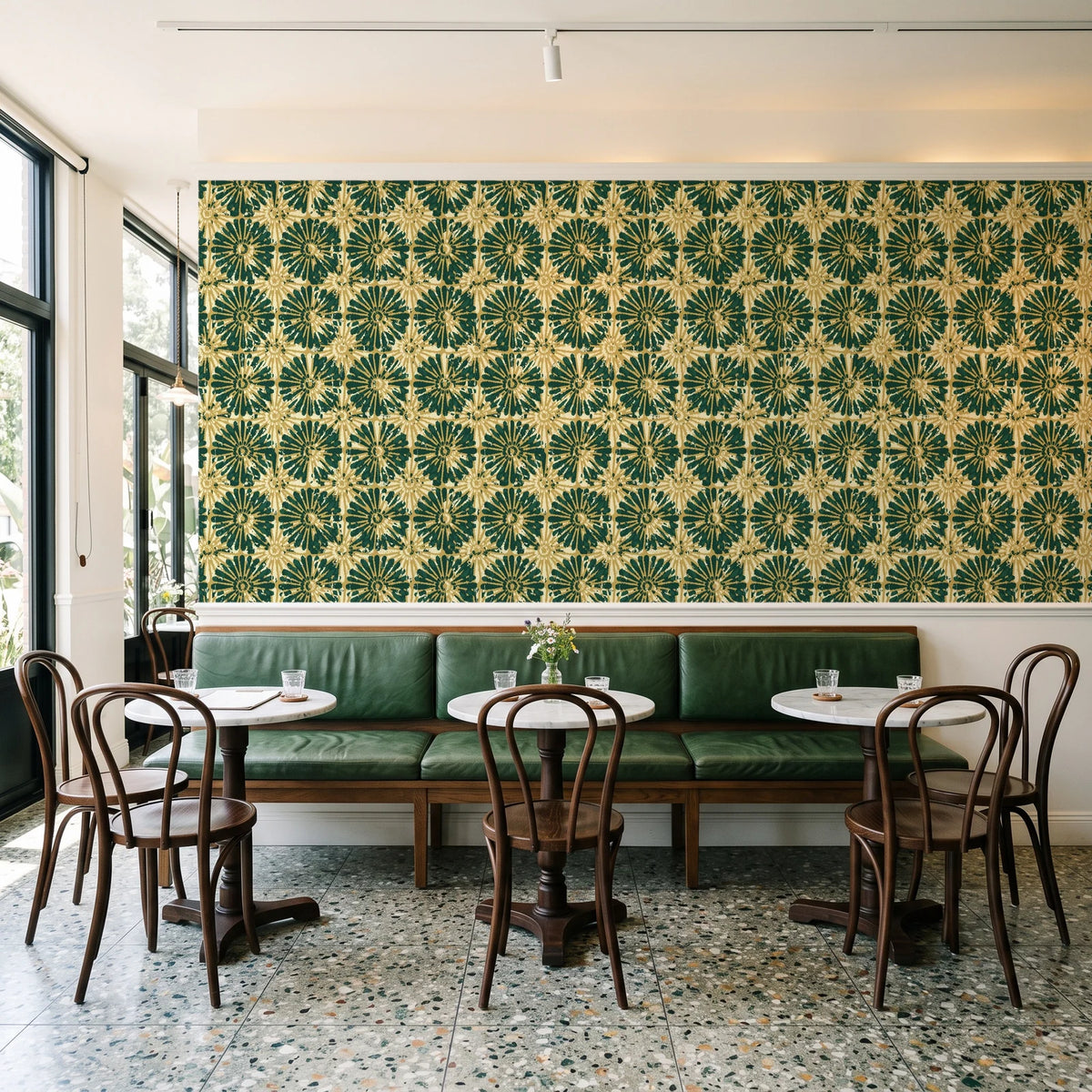 Solar Ritual Emerald floral wallpaper above a green leather banquette in a sunlit neighborhood cafe