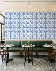 Solar Ritual Indigo floral wallpaper above a green leather banquette in a sunlit neighborhood cafe