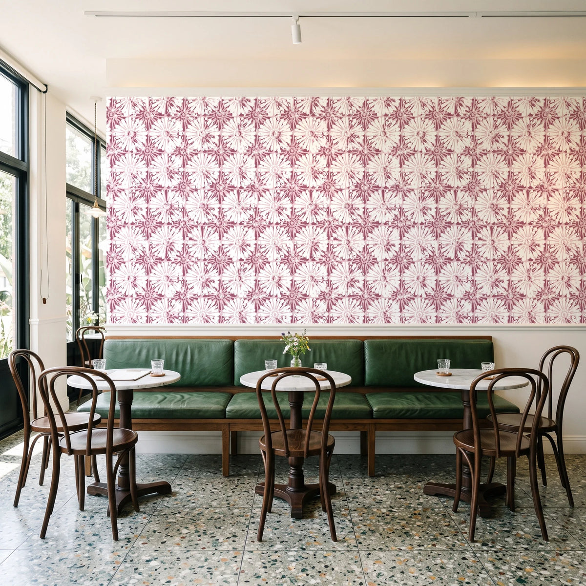 Solar Ritual Rosewood floral wallpaper above a green leather banquette in a sunlit neighborhood cafe