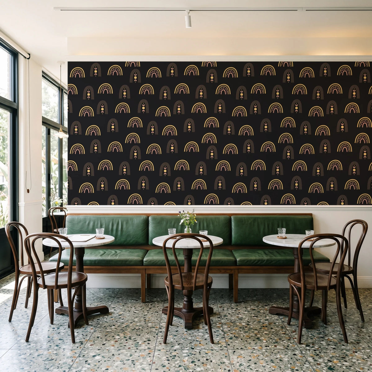Solstice Rite Eclipse boho rainbow wallpaper above a green leather banquette in a sunlit neighborhood cafe