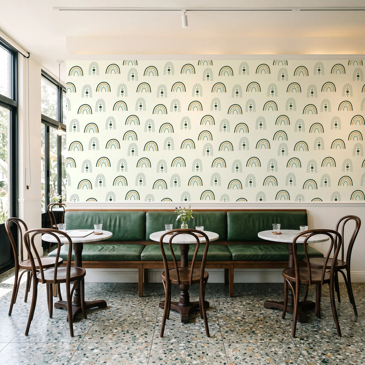 Solstice Rite Forest boho rainbow wallpaper above a green leather banquette in a sunlit neighborhood cafe