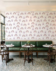 Solstice Rite Plum boho rainbow wallpaper above a green leather banquette in a sunlit neighborhood cafe