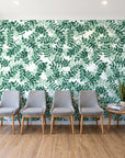 Still Morning Emerald foliage wallpaper behind a row of upholstered chairs in a bright clinic waiting room
