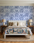 Tranquil Flora Indigo floral damask wallpaper behind a white cottage bed with a patchwork quilt in a cozy cottagecore bedroom