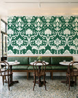 Twilight Garden Veil Emerald damask wallpaper above a green leather banquette in a sunlit neighborhood cafe