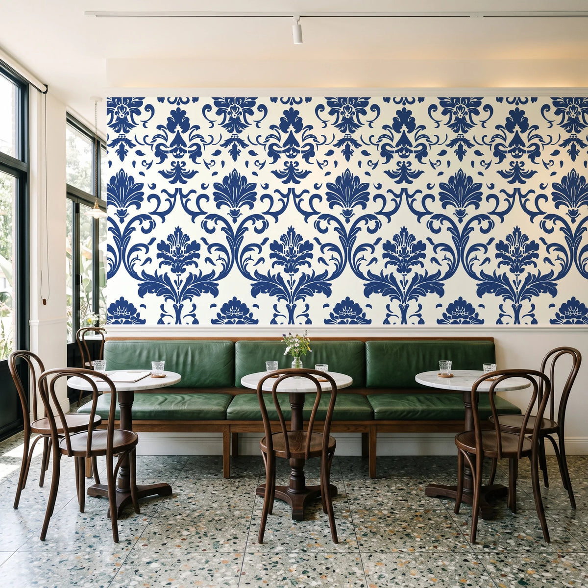 Twilight Garden Veil Indigo damask wallpaper above a green leather banquette in a sunlit neighborhood cafe