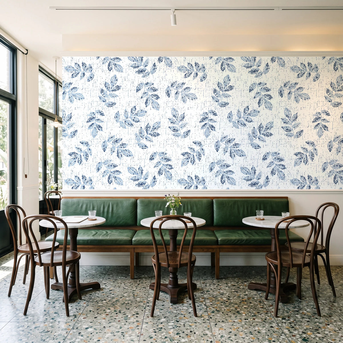 Verdant Scatter Navy tossed leaf wallpaper above a green leather banquette in a sunlit neighborhood cafe