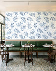 Verdant Scatter Navy tossed leaf wallpaper above a green leather banquette in a sunlit neighborhood cafe