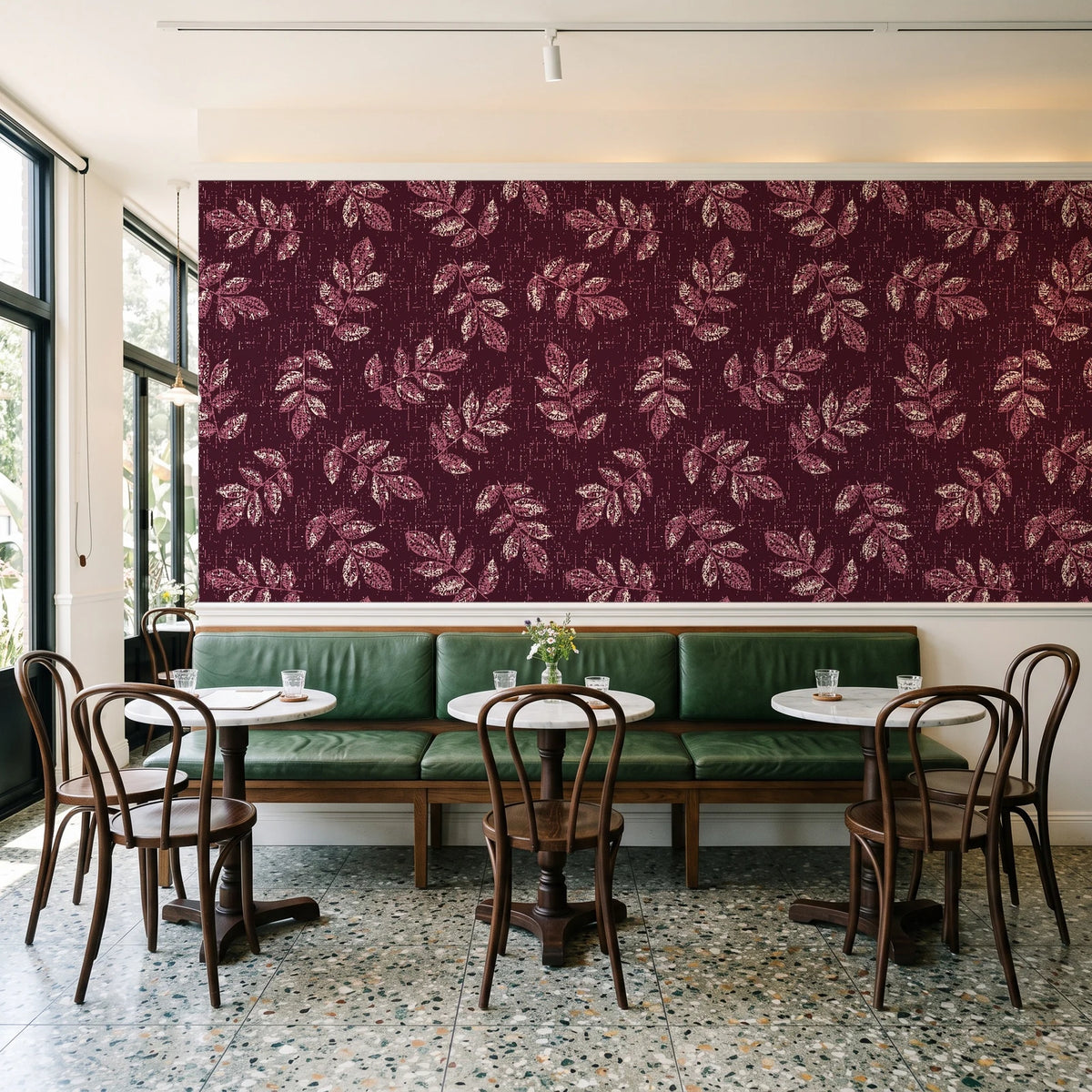 Verdant Scatter Oxblood tossed leaf wallpaper above a green leather banquette in a sunlit neighborhood cafe