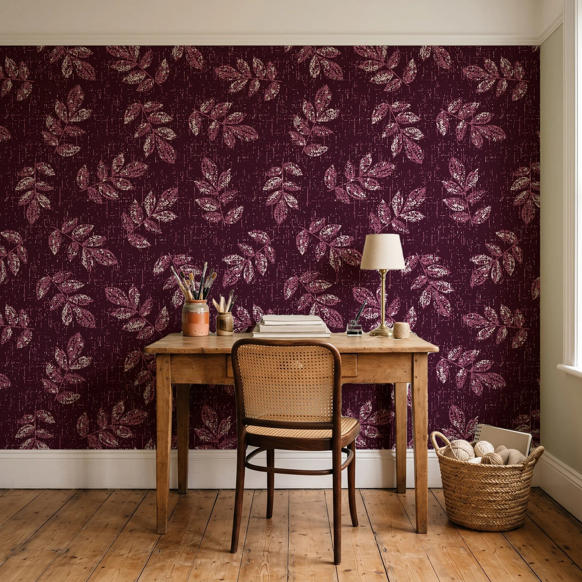 Verdant Scatter Oxblood tossed leaf wallpaper behind a vintage writing desk in a cozy craft-room home office