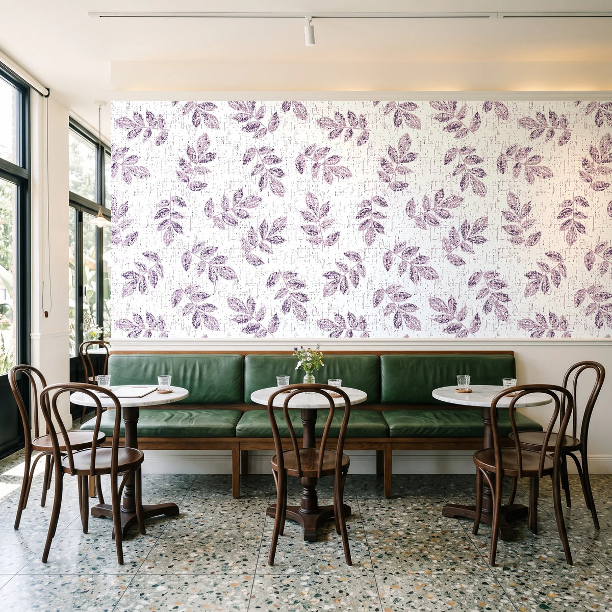 Verdant Scatter Plum tossed leaf wallpaper above a green leather banquette in a sunlit neighborhood cafe