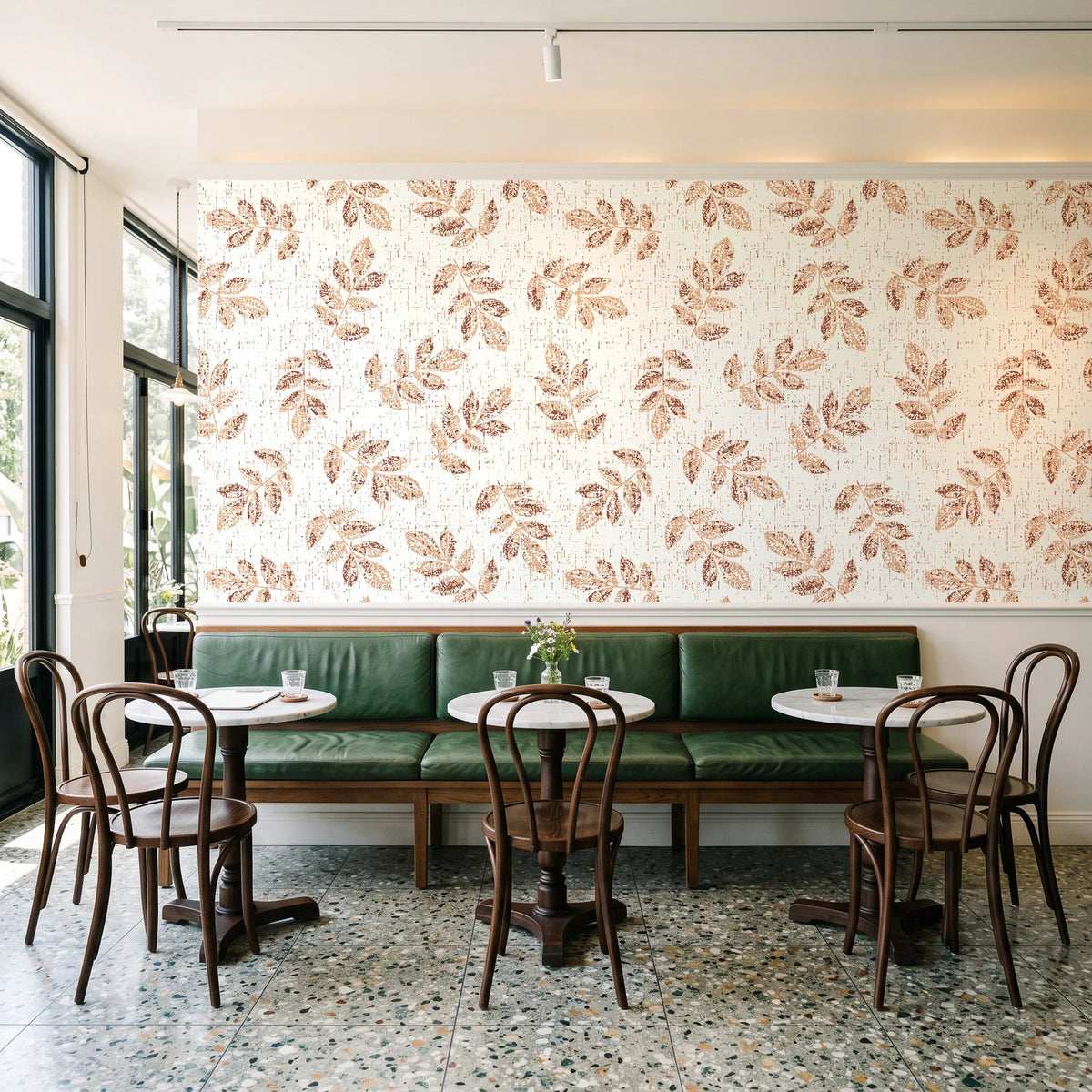 Verdant Scatter Terracotta tossed leaf wallpaper above a green leather banquette in a sunlit neighborhood cafe