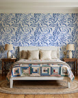 Willow Trace Indigo willow vine wallpaper behind a white cottage bed with a patchwork quilt in a cozy cottagecore bedroom
