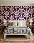 Woodland Blossom Veil Oxblood damask wallpaper behind a white cottage bed with a patchwork quilt in a cozy cottagecore bedroom